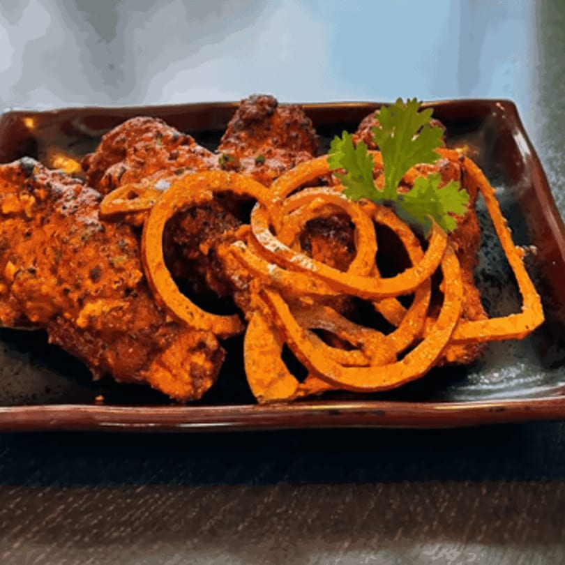 Spicy chicken wings with onion rings and a sprig of cilantro on a dark rectangular plate.
